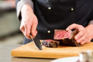 Chef chopping meat on chopping board as it is a high risk food