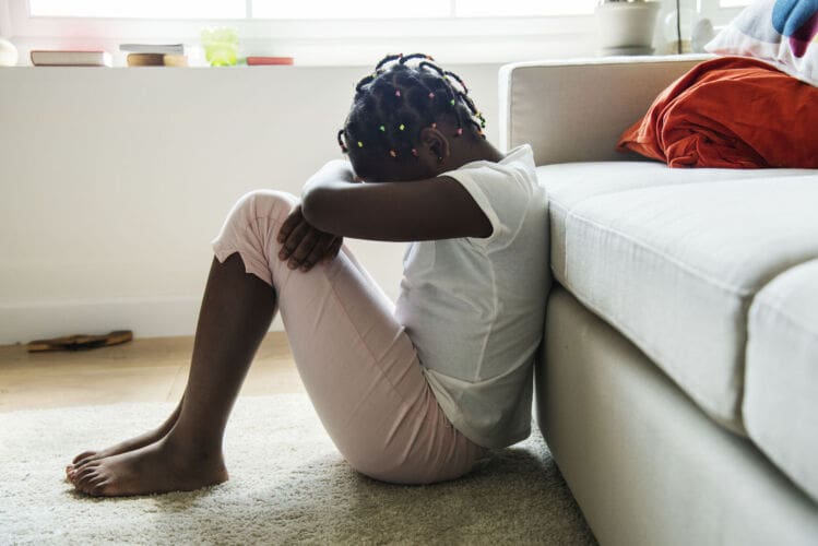 Upset young girl sat on the floor with low self-esteem after having female circumcision carried out when she was younger